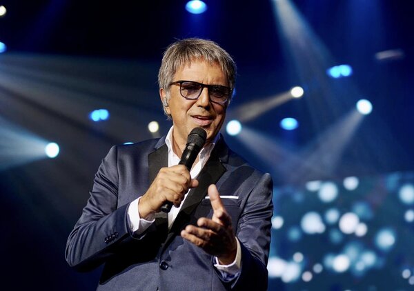 Fernando Pereira atua em palco, segurando um microfone durante um espetáculo.